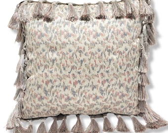 May include: A decorative square pillow with a floral pattern in shades of pink, blue, and beige. The pillow is trimmed with a fringe of tassels in a matching color palette, adding a touch of elegance to the design.