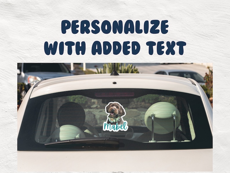 May include: A white car with a rear window sticker featuring a brown dog with a blue collar and a flower crown. The sticker also includes the name "Mabel" in teal text.