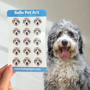 May include: A rectangular sticker sheet featuring fifteen circular stickers, each displaying a portrait of a fluffy dog with white, grey, and brown fur. The blue header reads BeBe Pet Art and the footer displays the website www.bebepetart.com.