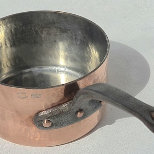 Puede incluir: Cacerola de cobre con acabado martillado y asa de hierro fundido. El interior es de color plateado. La cacerola es redonda y tiene un solo asa sujeta con remaches. Fabricado en Francia.