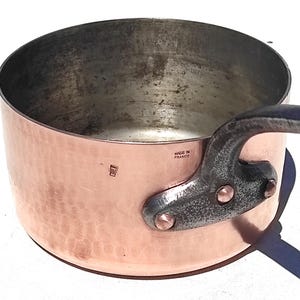 May include: A copper saucepan with a hammered finish, featuring a dark metal handle secured with rivets. The words "MADE IN FRANCE" are stamped on the side. A classic kitchenware item.