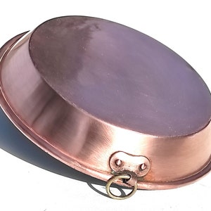 May include: A copper oval pan with a rounded rim and a shiny surface. It features a small handle with a ring for hanging. The pan is likely for cooking and has a classic, vintage look. The pan's dimensions are in centimeters.