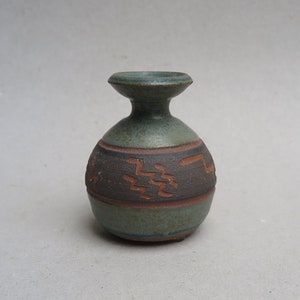 May include: A small, green ceramic vase with a brown band and geometric designs. The vase has a rounded body and a flared lip.