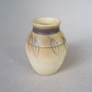May include: A small, cream-colored ceramic vase with a brown band around the top and a leaf design.