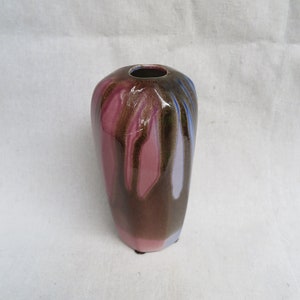 May include: A small, ceramic vase with a unique, abstract design. The vase is a deep pink color with brown and blue streaks running vertically down the surface.