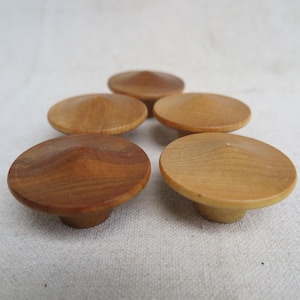 May include: Five wooden cabinet knobs with a rounded, mushroom-like design. The knobs are made of light and dark brown wood, with a smooth, polished finish. The knobs are arranged in a slightly offset pattern.