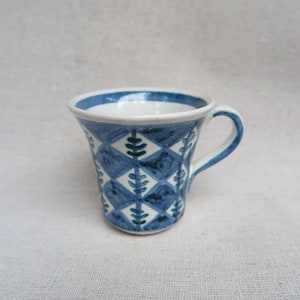 May include: A small, white ceramic mug with a blue and white geometric pattern. The mug has a flared rim and a handle.
