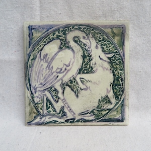 May include: Square ceramic tile with a hand-painted design featuring a bird and a deer in a circular frame. The artwork uses shades of white, green, and purple. The tile is approximately 6 inches square.