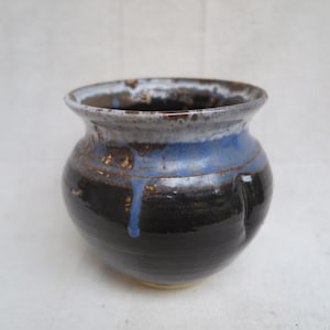 May include: A handmade ceramic pot with a dark blue and black glaze. The rim is a lighter color, and there are blue drips down the side. The pot has a rounded shape and a wide opening, perfect for holding small items or as a decorative piece.