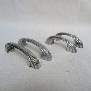 May include: Four silver-toned cabinet pulls with a curved, arched design. The pulls have a smooth, polished finish.