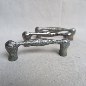 May include: Three silver metal drawer pulls with a textured, hammered finish. The pulls have a unique, organic shape.