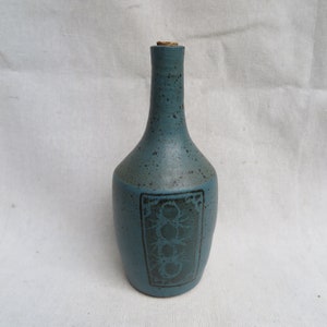 May include: A blue ceramic bottle with a cork stopper and a black design. The design features a geometric pattern with circles and lines.