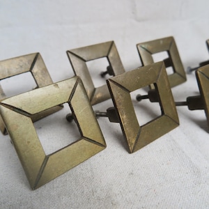 May include: A collection of antique brass square drawer pulls. Each pull features a hollow square design with a small screw for attachment. The brass has a vintage patina, suggesting age and use. Ideal for furniture restoration or adding a touch of vintage charm.