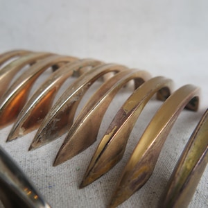 May include: A collection of vintage brass cabinet pulls. The pulls have a curved, arching design with a pointed end. The brass has a warm, golden hue with some areas showing signs of wear and age. The hardware is likely for furniture restoration.