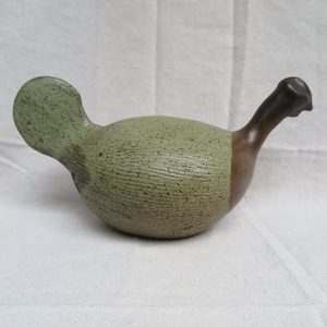 May include: A ceramic bird figurine with a green and brown glaze. The bird has a rounded body and a long neck.