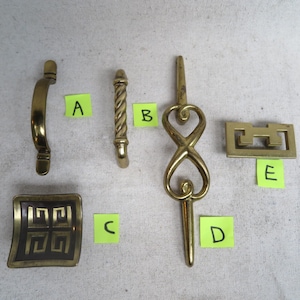 May include: An assortment of vintage brass hardware, including cabinet pulls and handles. The collection features various designs: a curved handle, a twisted column, an infinity-shaped pull, a rectangular handle, and a square plate with a geometric pattern.