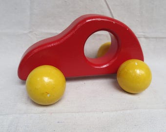 May include: A red wooden toy car with yellow wheels. The car has a hole in the middle for a child to hold.