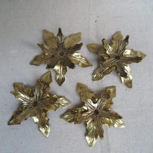 May include: Four brass leaf-shaped decorative hardware pieces. Each piece has a central hole and detailed leaf veining. The leaves are a warm gold color and appear to be vintage or antique. They are arranged on a neutral background.