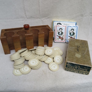 May include: A vintage poker set featuring a wooden chip holder, playing cards, and a box of poker chips. The chips are off-white with a clover design. The playing cards have a portrait of a man with a violin. The box reads "100 U.S. Poker Chips 1 inch".