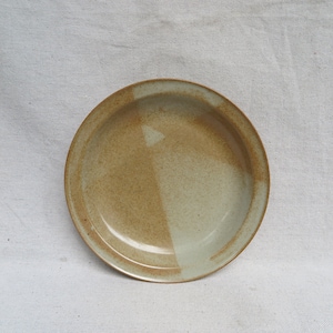 May include: A ceramic plate with a light brown and green glaze. The plate has a slightly raised rim and a smooth, rounded bottom.
