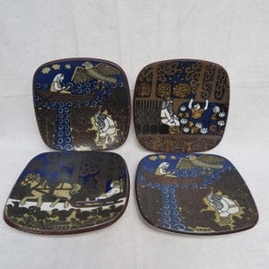 May include: Set of four square ceramic plates with rounded corners. Each plate features a unique illustration in shades of blue, brown, and white, depicting figures, trees, and animals. The plates have a dark brown border.