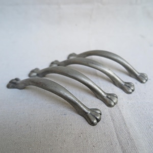 May include: Four antique-style cabinet pulls with a pewter finish. Each pull has a curved handle and a paw-shaped design at the ends. The pulls are arranged on a white surface.