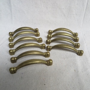 May include: Ten antique brass cabinet door pulls with a curved shape and rounded ends.