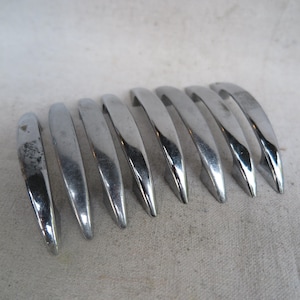 May include: A collection of eight curved, chrome-finished cabinet pulls. Each pull has a smooth, polished surface and a slightly pointed end. The pulls are arranged in a row against a neutral background.