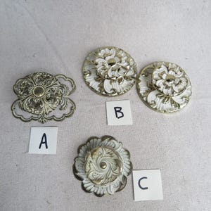 May include: An assortment of decorative hardware, including drawer pulls and a cabinet pull. The pulls feature ornate floral designs in gold and white. The hardware is labeled A, B, and C.