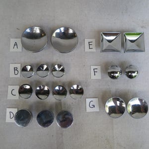 May include: An assortment of shiny, silver-colored metal objects, including various shapes like circles, squares, and half-spheres. The objects are arranged in rows and columns, with lettered labels next to each group.