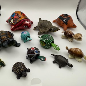 Könnte beinhalten: Eine Sammlung dekorativer Schildkrötenfiguren in verschiedenen Größen und Stilen. Die Schildkröten weisen verschiedene Farben und Muster auf, darunter bemalte Designs, strukturierte Panzer und einzigartige Ausdrücke. Einige Schildkröten haben ihren Kopf und ihre Gliedmaßen ausgestreckt.