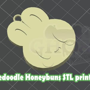 May include: A light yellow, 3D-printed design of a cartoon character's face with closed eyes and a smiling mouth. The design has a loop at the top for hanging. Text at the bottom reads "Rosedoodle Honeybuns STL print file."