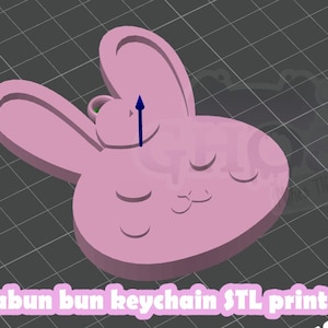 May include: A light pink bunny-shaped keychain with closed eyes and a small loop for attachment. The keychain has a 3D printed appearance and the text "Shiabun bun keychain STL print file" is visible at the bottom.