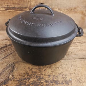 May include: A black cast iron roaster with a lid. The lid has a handle and the words "PEDROP ROASTER" and "No 9" are embossed on the lid. The roaster is sitting on a wooden surface.