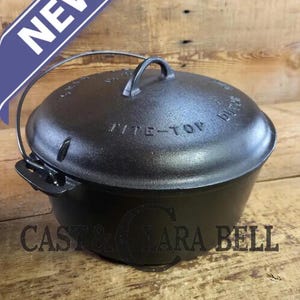May include: A black cast iron Dutch oven with a lid and handle. The lid is embossed with the words "Tite-Top" and "Cast & Lara Bell" is printed on the side. A blue banner with the word "NEW" is in the upper left corner.