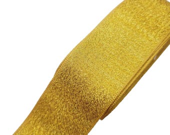 May include: Close-up of a gold ribbon with a textured surface. The ribbon is folded over itself, revealing its thickness. The colour is a bright, metallic gold, and the material appears to be fabric. The ribbon is against a white background.