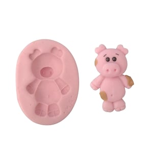 May include: A pink silicone mold and a small, pink pig figurine. The mold is oval-shaped with an embossed pig design. The pig figurine has brown spots and is standing upright.
