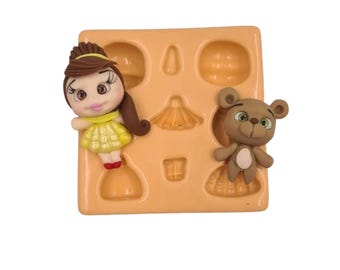 Puede incluir: Un molde de silicona con siete cavidades. El molde presenta una princesa, un oso, un vestido, una corona y tres formas más. El molde es de color marrón claro y tiene una superficie lisa.