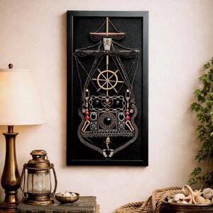 Pode incluir: Uma obra de arte emoldurada que retrata um navio, feita de v&aacute;rios enfeites met&aacute;licos. A obra apresenta um fundo preto com detalhes dourados, prateados e vermelhos, incluindo um leme, correntes e elementos decorativos. A moldura &eacute; preta.