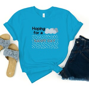 May include: A turquoise blue t-shirt with the text "Hoping for a rainy day" and a gray cloud with raindrops falling from it.