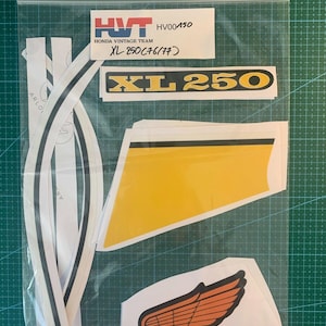 Op de afbeelding: Een set motorfiets stickers voor een Honda XL 250. De stickers zijn wit met zwarte en gele accenten. De set bevat de woorden "XL 250" en "Honda" samen met een vleugellogo.