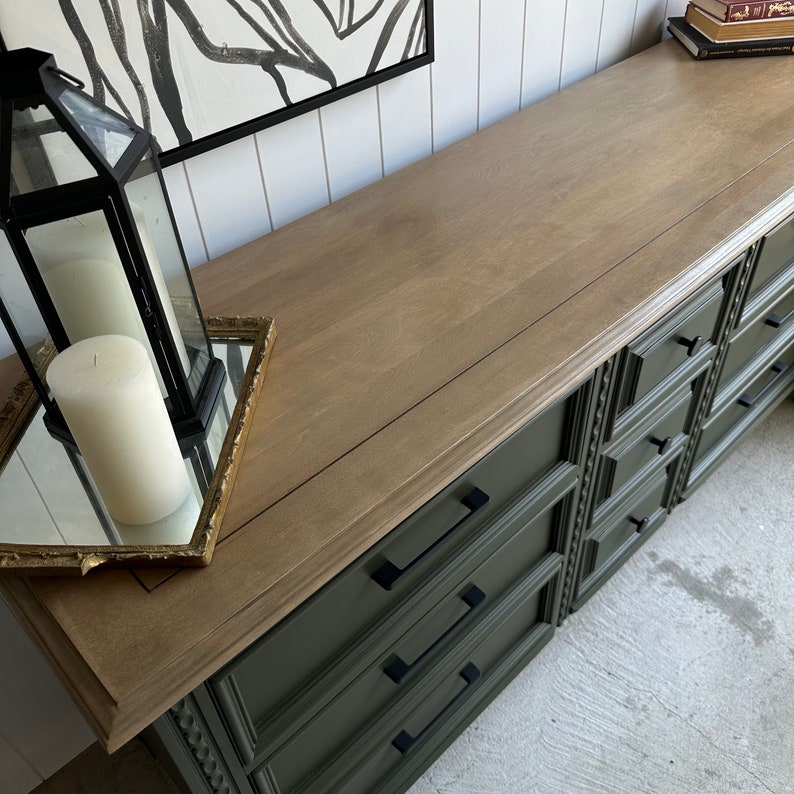 May include: A vintage dresser with a light wood top and dark green painted drawers. The dresser has ornate details and black drawer pulls.