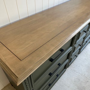 May include: A green dresser with black drawer pulls and a light brown wood top. The top has a dark brown border around the edge.