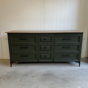 May include: A dark green dresser with eight drawers and black hardware. The dresser has a light wood top and black metal legs.