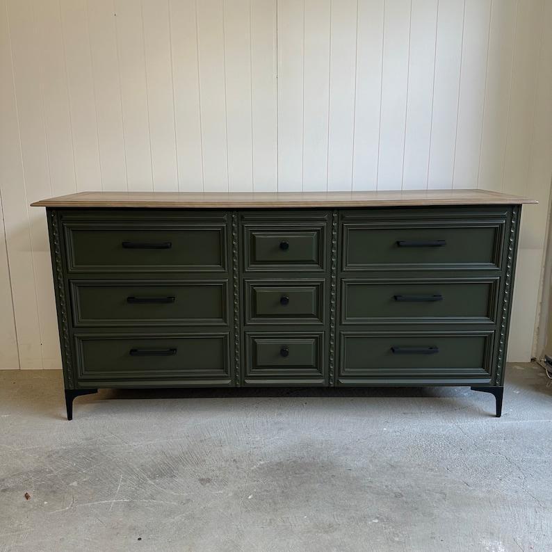 May include: A dark green dresser with eight drawers and black hardware. The dresser has a light wood top and black metal legs.