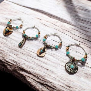 May include: Four silver and turquoise glass charm rings with different charms. The charms include a heart, a teardrop, a teardrop with a cross, and a round charm with a turquoise stone.