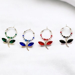 Puede incluir: Cuatro pares de pendientes de aro de plata con dijes de libélula. Las libélulas tienen alas de cristal en verde, azul, rojo y negro.