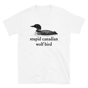 Pode incluir: Camiseta branca com uma ilustração a preto e branco de um mergulhão com olhos vermelhos. O texto "stupid canadian wolf bird" está impresso em baixo a preto. A camisa é feita de um material macio e leve.