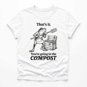 Könnte beinhalten: Weißes T-Shirt mit einer Schwarz-Weiß-Illustration eines Frosches mit Schürze und Heugabel. Der Text auf dem Shirt lautet: "That's it. You're going in the COMPOST."