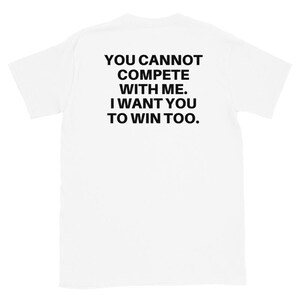 Könnte beinhalten: Weißes T-Shirt mit dem schwarzen Text: "YOU CANNOT COMPETE WITH ME. I WANT YOU TO WIN TOO." Das T-Shirt hat kurze Ärmel und einen Rundhalsausschnitt.